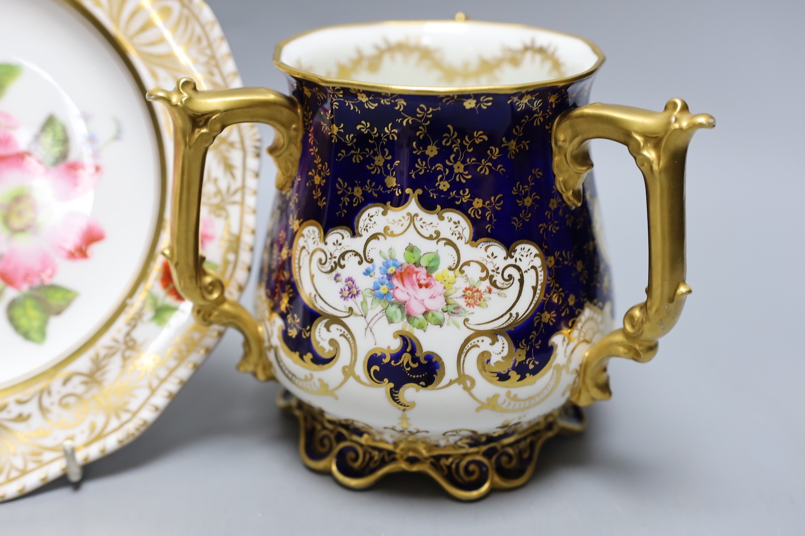 A Derby King Street plate by Harry Sampson Hancock monogrammed verso 'II' red S and H mark and a Royal Crown Derby three handled loving cups